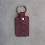 Sangria wine-red leather keychain debossed with a vizsla and the words Velcro DOG, on gray concrete