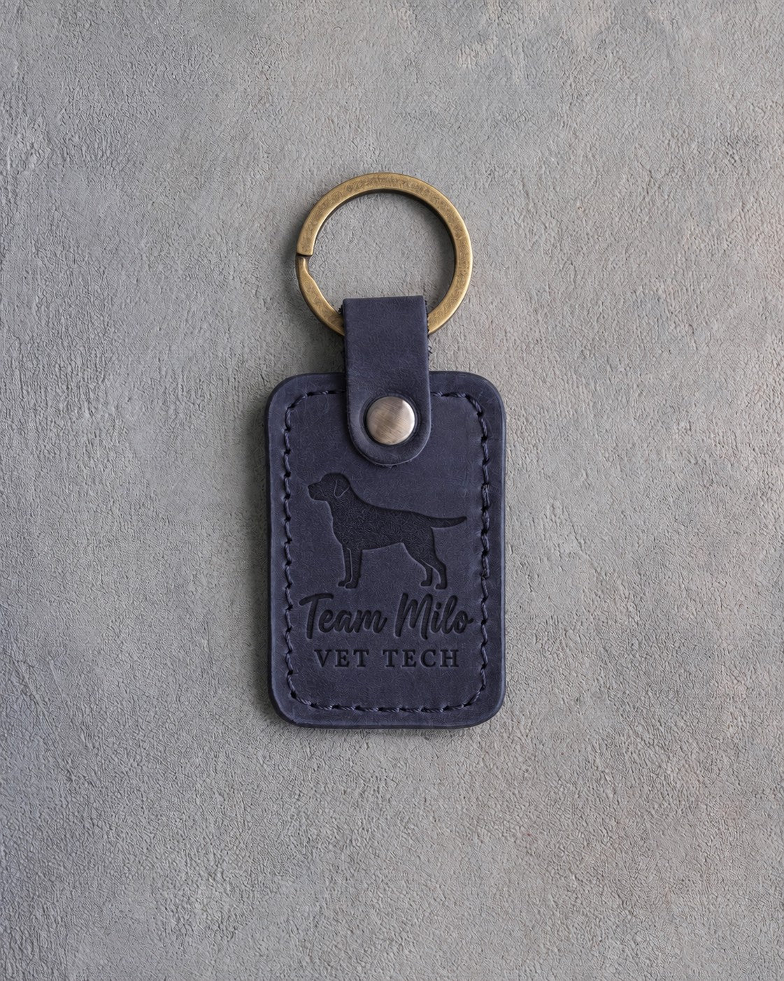 Blueberry navy leather keychain debossed with a Labrador above Team Milo and VET TECH, on gray concrete