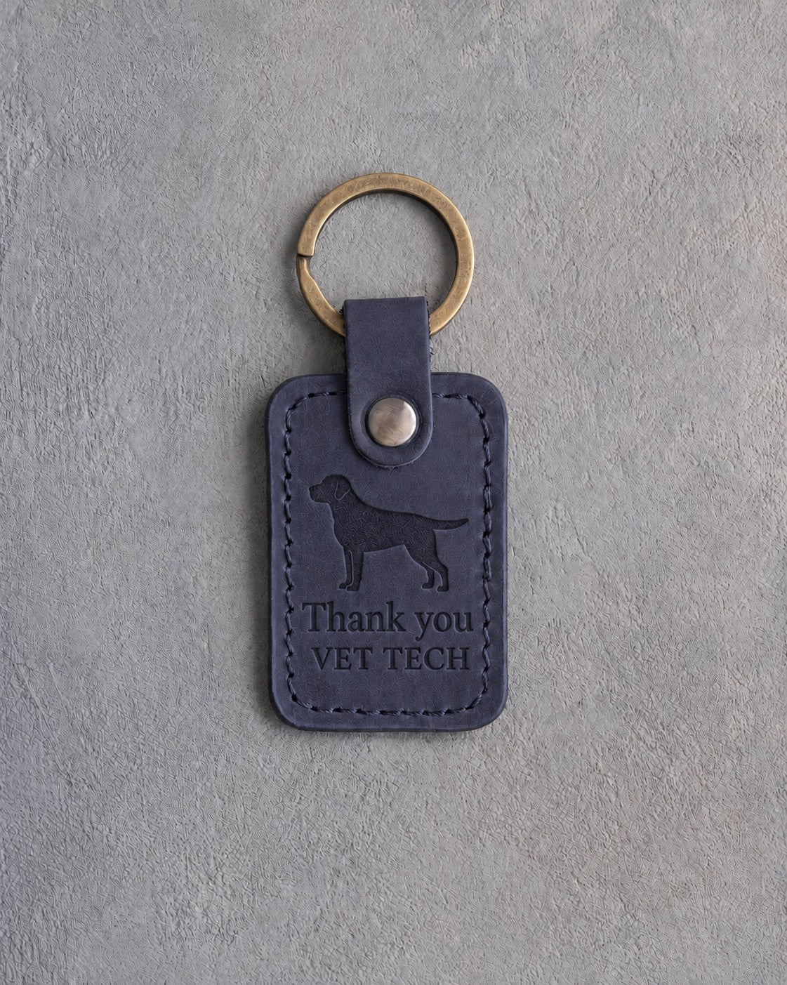 Blueberry navy leather keychain debossed with a Labrador above Thank you and VET TECH, on gray concrete