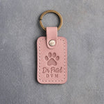 Blush pink leather keychain debossed with a paw print above the name Dr Patel and DVM, on gray plaster