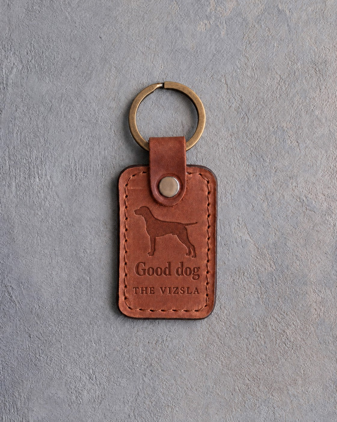 Arizona tan leather keychain debossed with a vizsla above Good dog and THE VIZSLA, on gray concrete