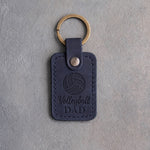 Blueberry navy leather keychain debossed with a volleyball and the words Volleyball DAD, on gray plaster