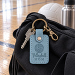 Turquoise Volleyball Mom keychain clipped to a backpack beside a volleyball in a tournament gym
