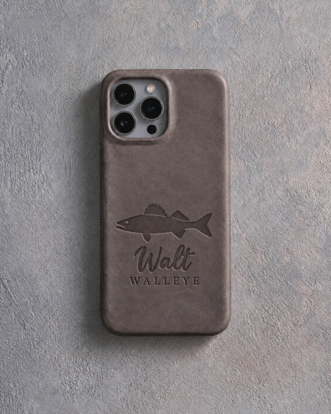 Back of a country gray leather iPhone case debossed with a walleye above Walt and WALLEYE below the camera, on gray plaster