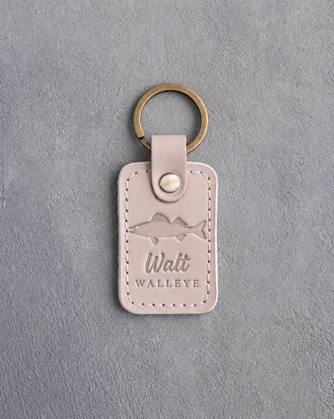 Gray sand leather keychain debossed with a walleye above Walt and WALLEYE, on gray plaster
