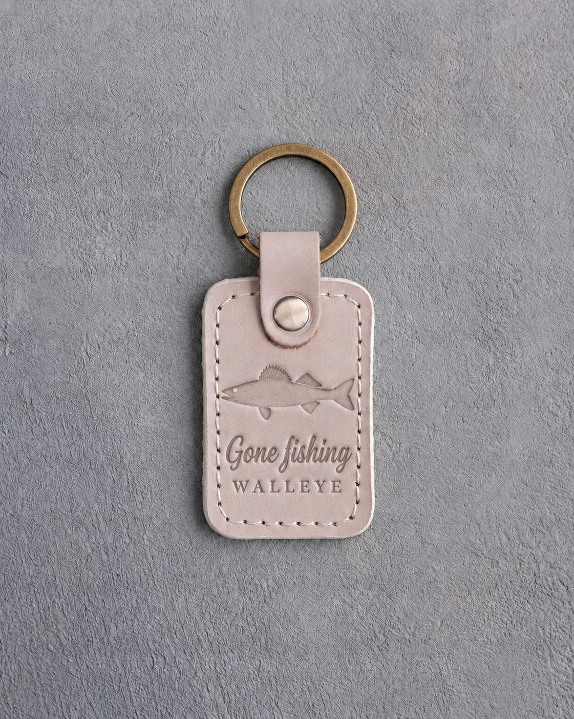 Gray sand leather keychain debossed with a walleye above Gone fishing and WALLEYE, on gray concrete