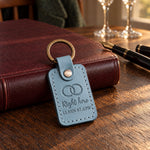 Right here coordinates keychain in turquoise leather on a dark oak table with two champagne flutes soft behind