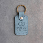 Turquoise leather keychain debossed with two interlocked wedding rings above Right here and 41.88N 87.63W, on gray concrete