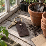 Dark brown Weed It and Reap keychain on a garden shed key beside a bucket of pulled weeds