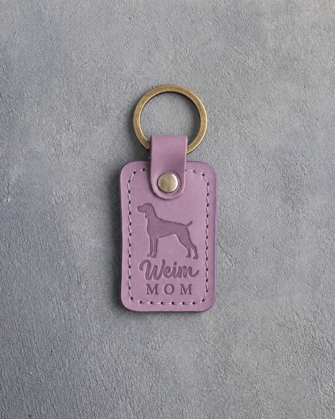 Lilac leather keychain with a debossed weimaraner and the words Weim MOM on gray concrete