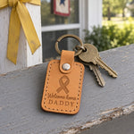Yellow Welcome Home Daddy keychain held up by a small child's hand in a bright airport terminal