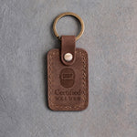 Sicilian brown leather keychain debossed with a front-view welding hood above the words Certified and WELDER, on gray concrete