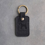 Black leather keychain debossed with a Miniature Schnauzer silhouette and the words Wet beard KISSES, on gray concrete