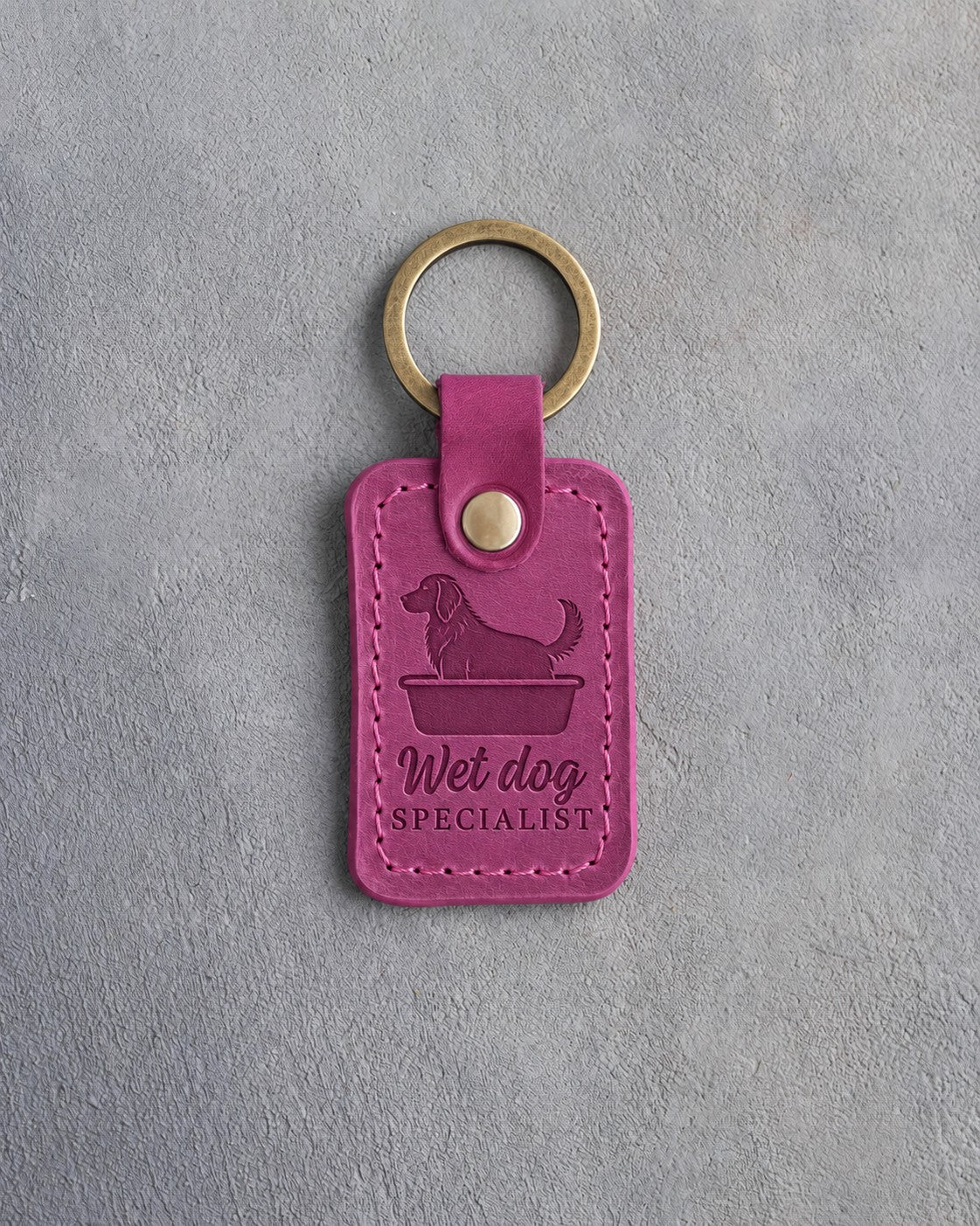 Fuchsia leather keychain debossed with a dog in a grooming tub and the words Wet dog SPECIALIST, on gray concrete