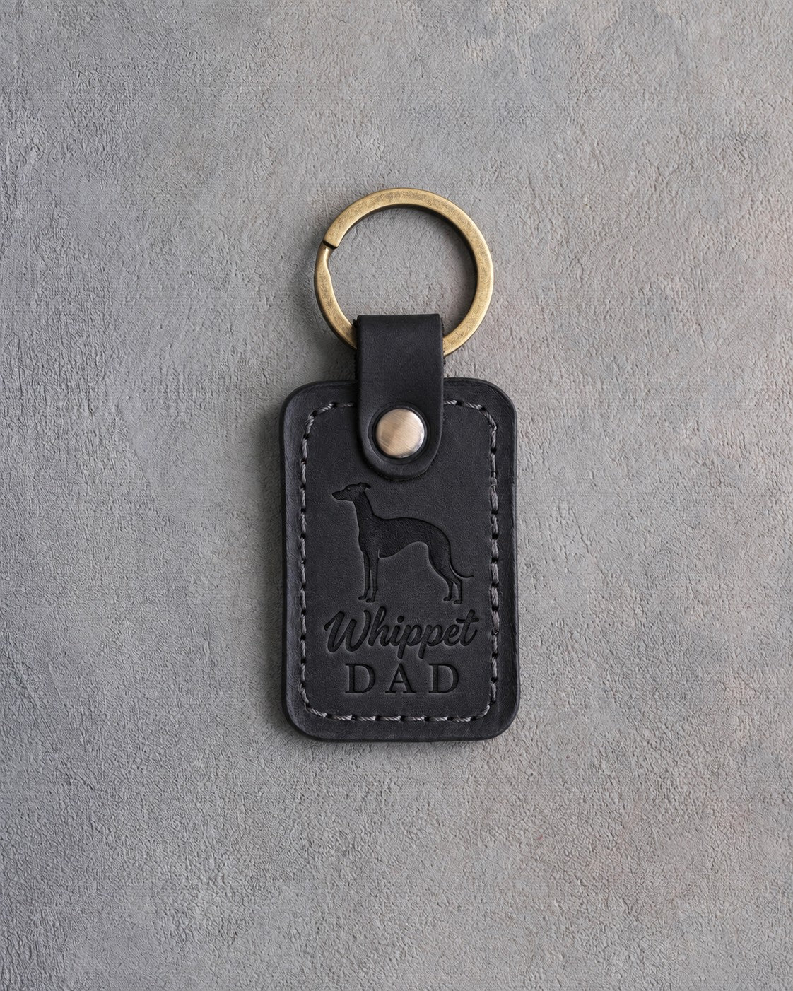Black leather keychain debossed with a whippet silhouette and Whippet DAD on gray concrete