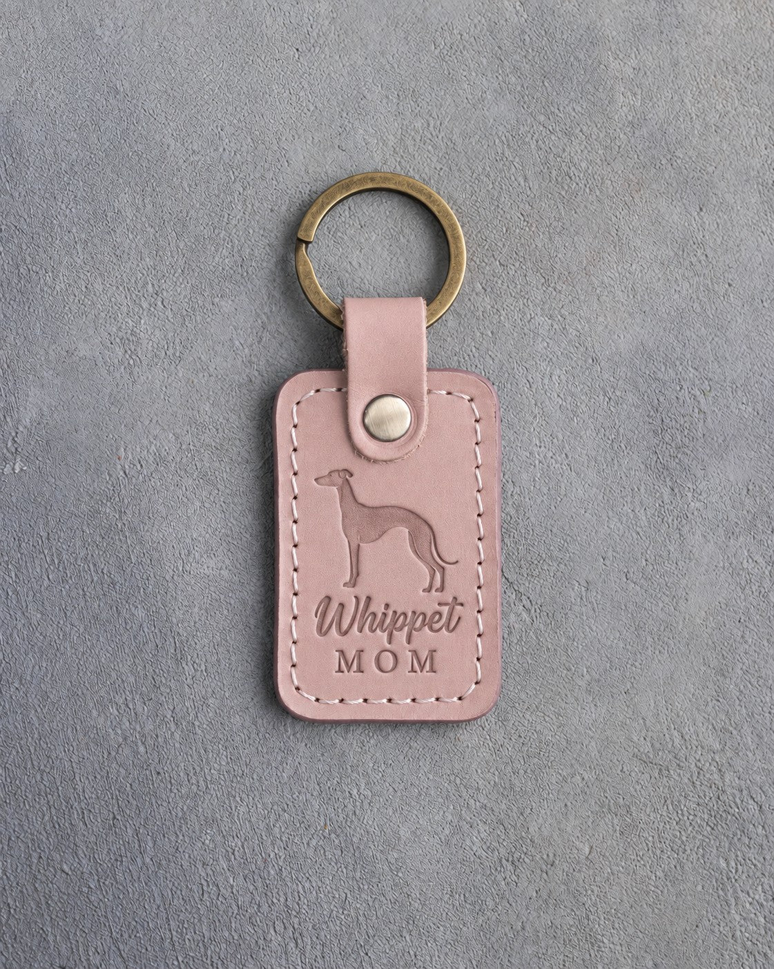 Blush pink leather keychain with a debossed whippet and the words Whippet MOM, on gray concrete