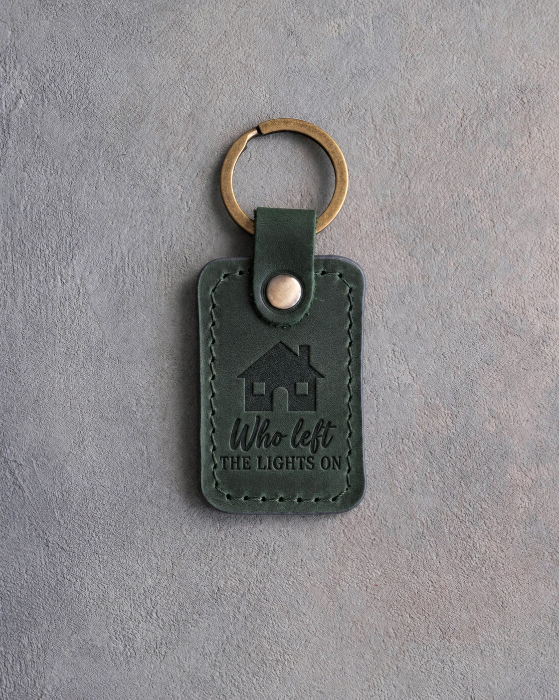 Forest green leather keychain debossed with a house with two lit windows above Who left and THE LIGHTS ON
