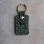 Forest green leather keychain debossed with a mixed breed dog and the words Who rescued WHO, on gray concrete