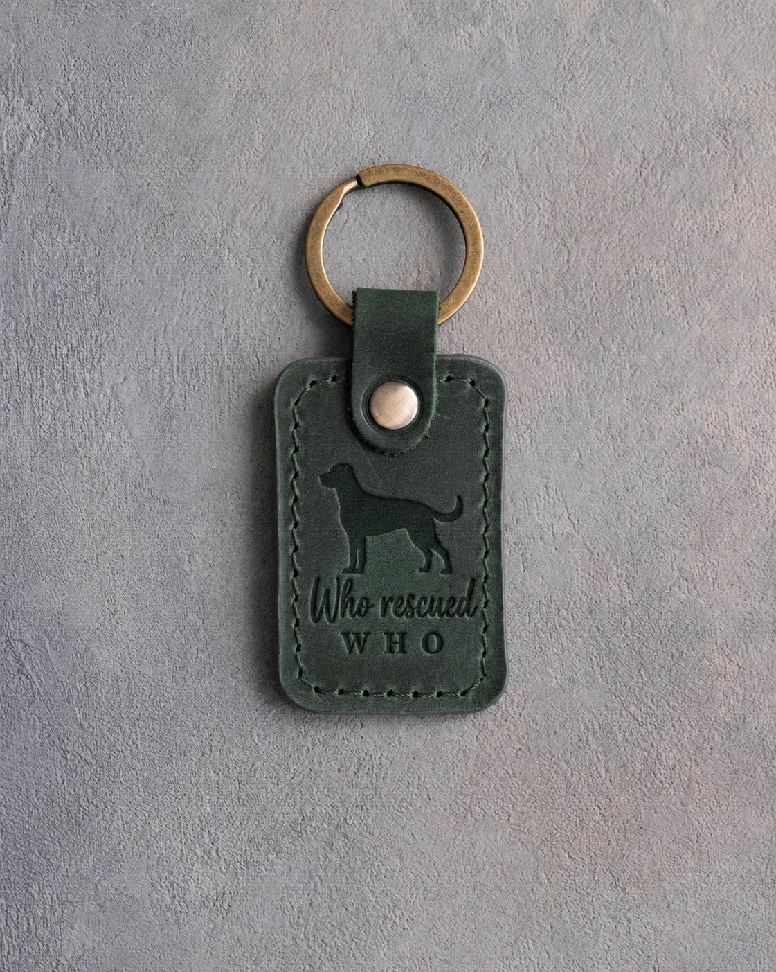 Forest green leather keychain debossed with a mixed breed dog and the words Who rescued WHO, on gray concrete