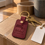 Wine red Wicked Homesick keychain on house keys beside a moving box and a folded scarf