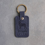 Blueberry navy leather keychain debossed with a Australian Shepherd silhouette and the words Wiggle BUTT, on gray concrete