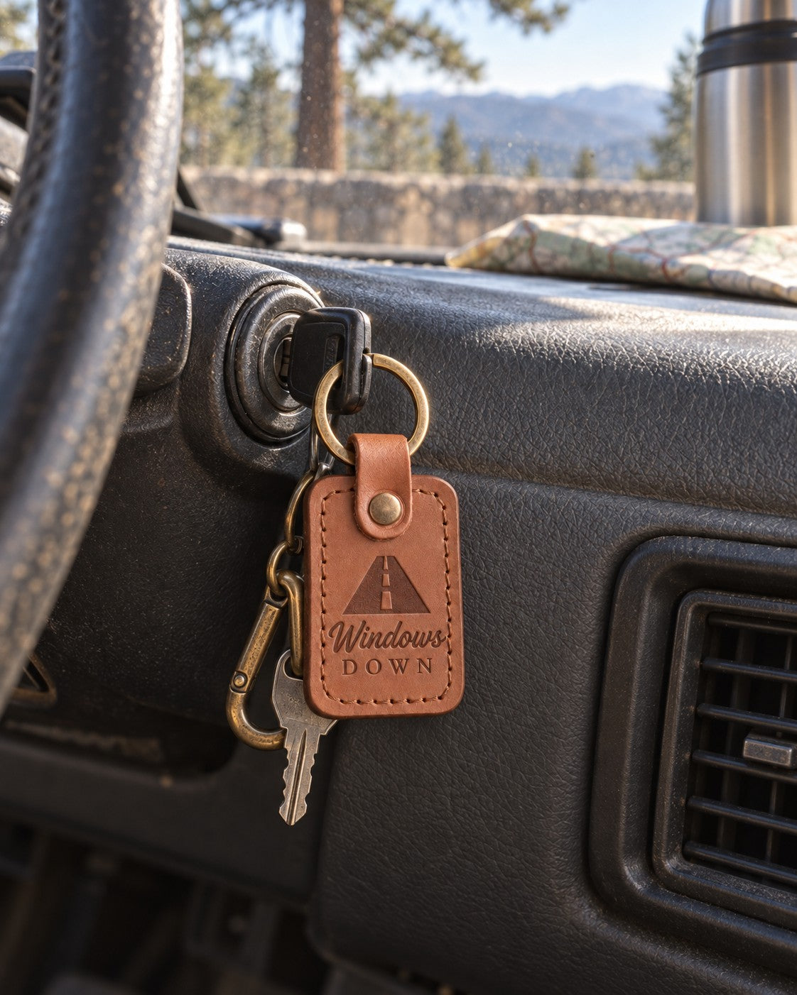 Caramel Windows Down keychain hanging from a car ignition with a desert highway through the windshield