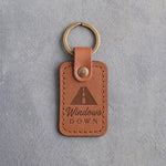 Caramel leather keychain debossed with an open road in perspective above Windows and DOWN, on gray concrete