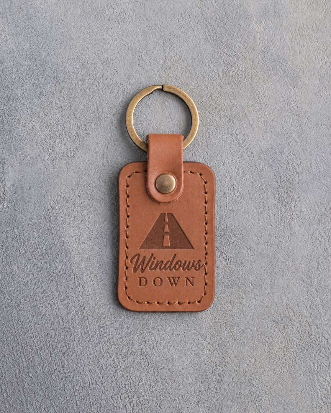 Caramel leather keychain debossed with an open road in perspective above Windows and DOWN, on gray concrete