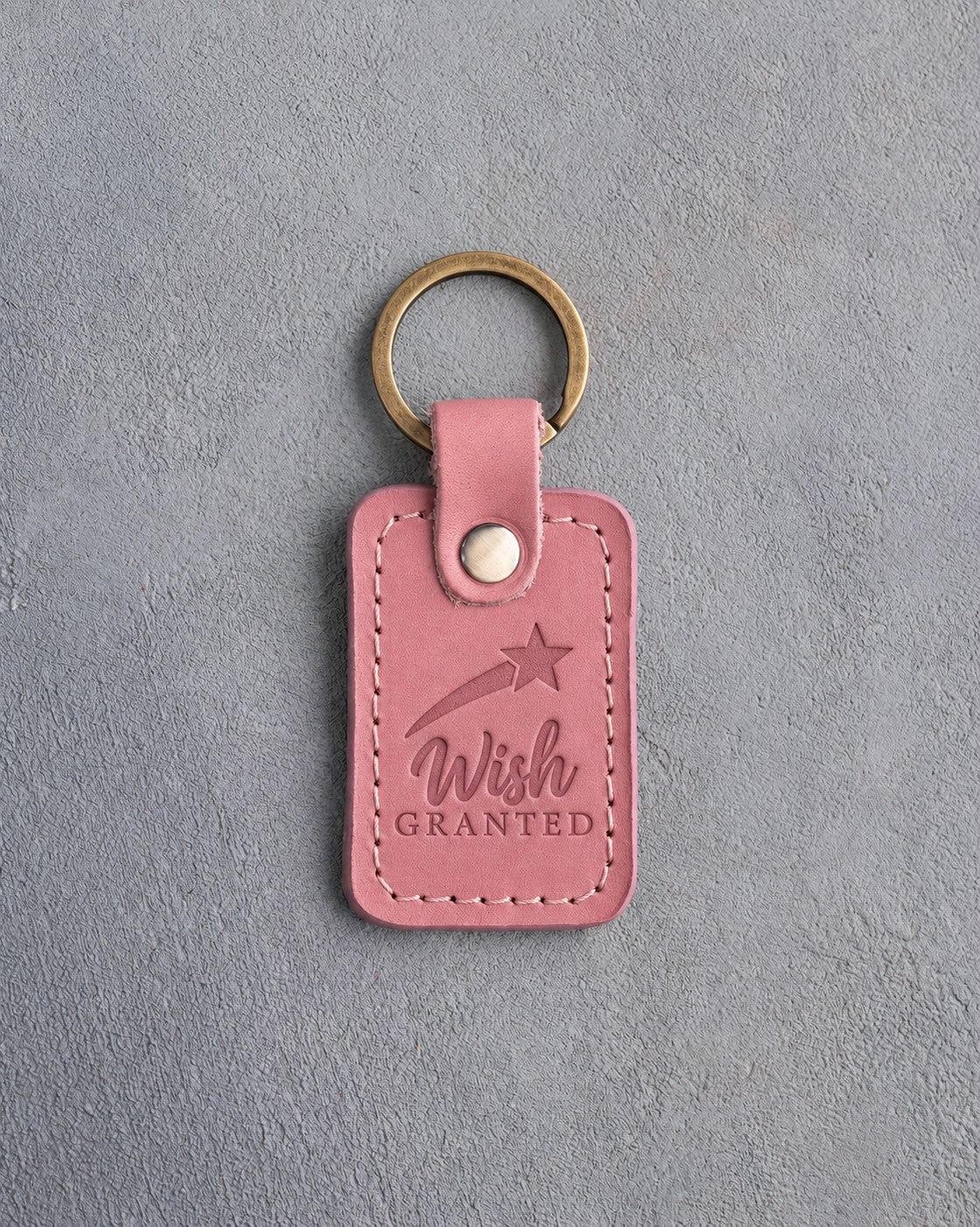 Rose pink leather keychain debossed with a shooting star above the words Wish GRANTED, on gray concrete