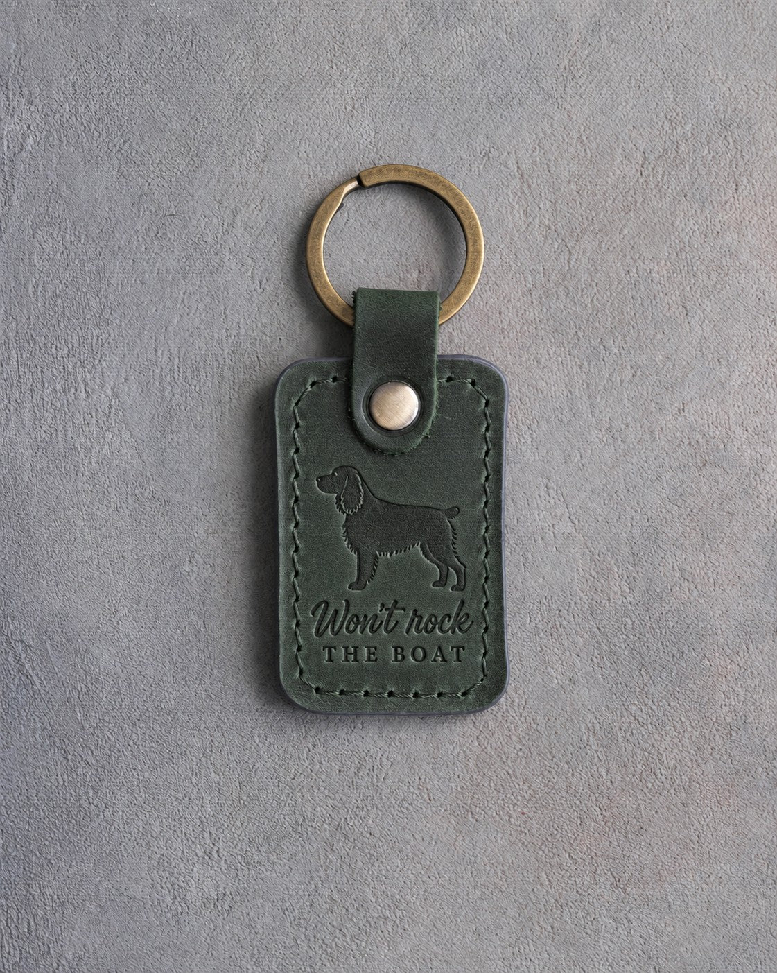 Forest green leather keychain debossed with a Boykin spaniel and the words Won't rock THE BOAT, on gray concrete