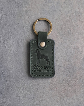 Forest green leather keychain debossed with a boxer silhouette and the words Woo woo SPOKEN HERE, on gray concrete