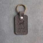 Country gray leather keychain debossed with an alert standing dog above Woof and THE DOG, on gray concrete