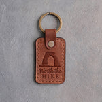 Sandy tan leather keychain debossed with a sandstone arch above Worth the and HIKE, on gray concrete