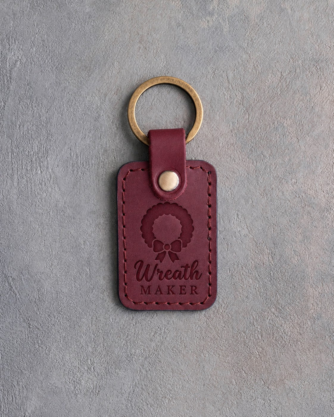 Sangria red leather keychain debossed with a leaf wreath and bow above Wreath MAKER, on gray concrete