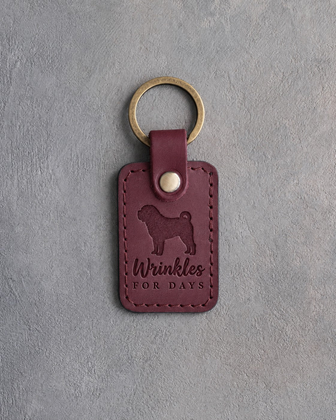 Sangria red leather keychain debossed with a Shar Pei silhouette and the words Wrinkles FOR DAYS, on gray concrete