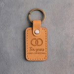 Indian Summer golden tan leather keychain debossed with two interlocked wedding rings above Ten years AND COUNTING, on gray concrete