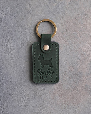 Forest green leather keychain debossed with a Yorkshire Terrier silhouette and the words Yorkie DAD, on gray concrete