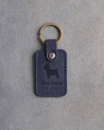 Blueberry navy leather keychain debossed with a Yorkshire Terrier silhouette above Best friend and THE YORKIE, on gray concrete