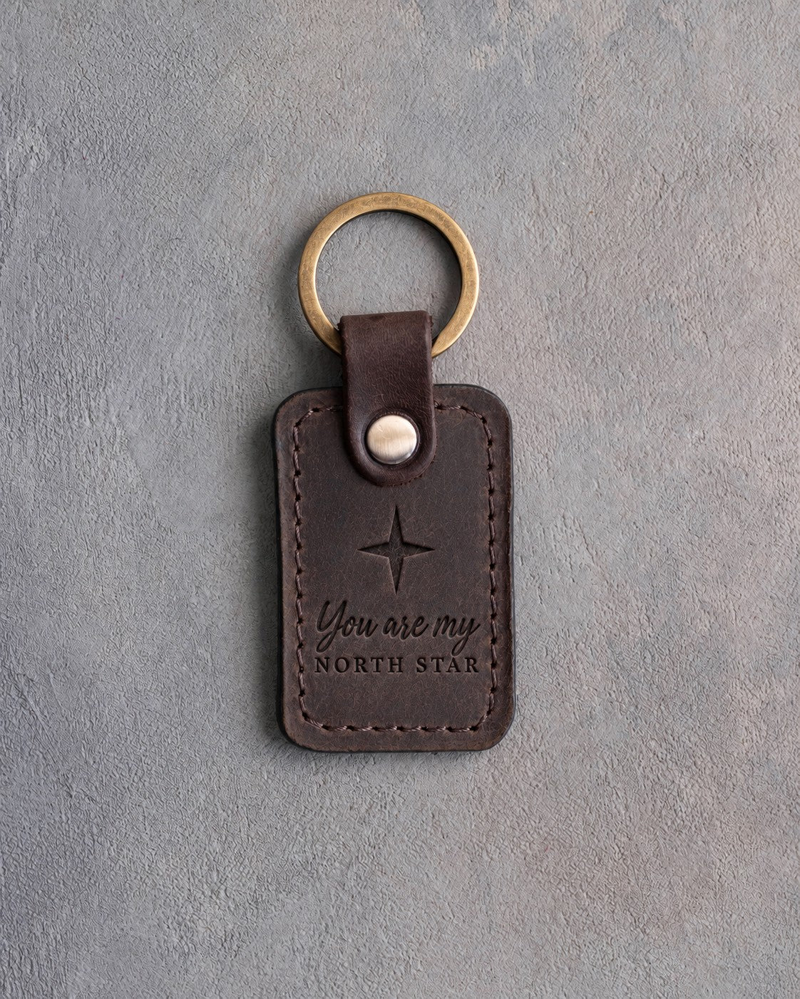 Dark espresso leather keychain debossed with a four-point star above You are my and NORTH STAR, on gray concrete