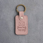 Blush pink leather keychain debossed with a sealed envelope above Yours truly and THE DOG, on gray concrete