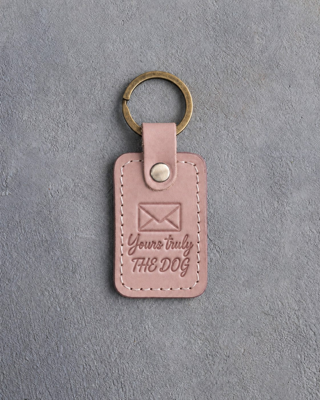 Blush pink leather keychain debossed with a sealed envelope above Yours truly and THE DOG, on gray concrete