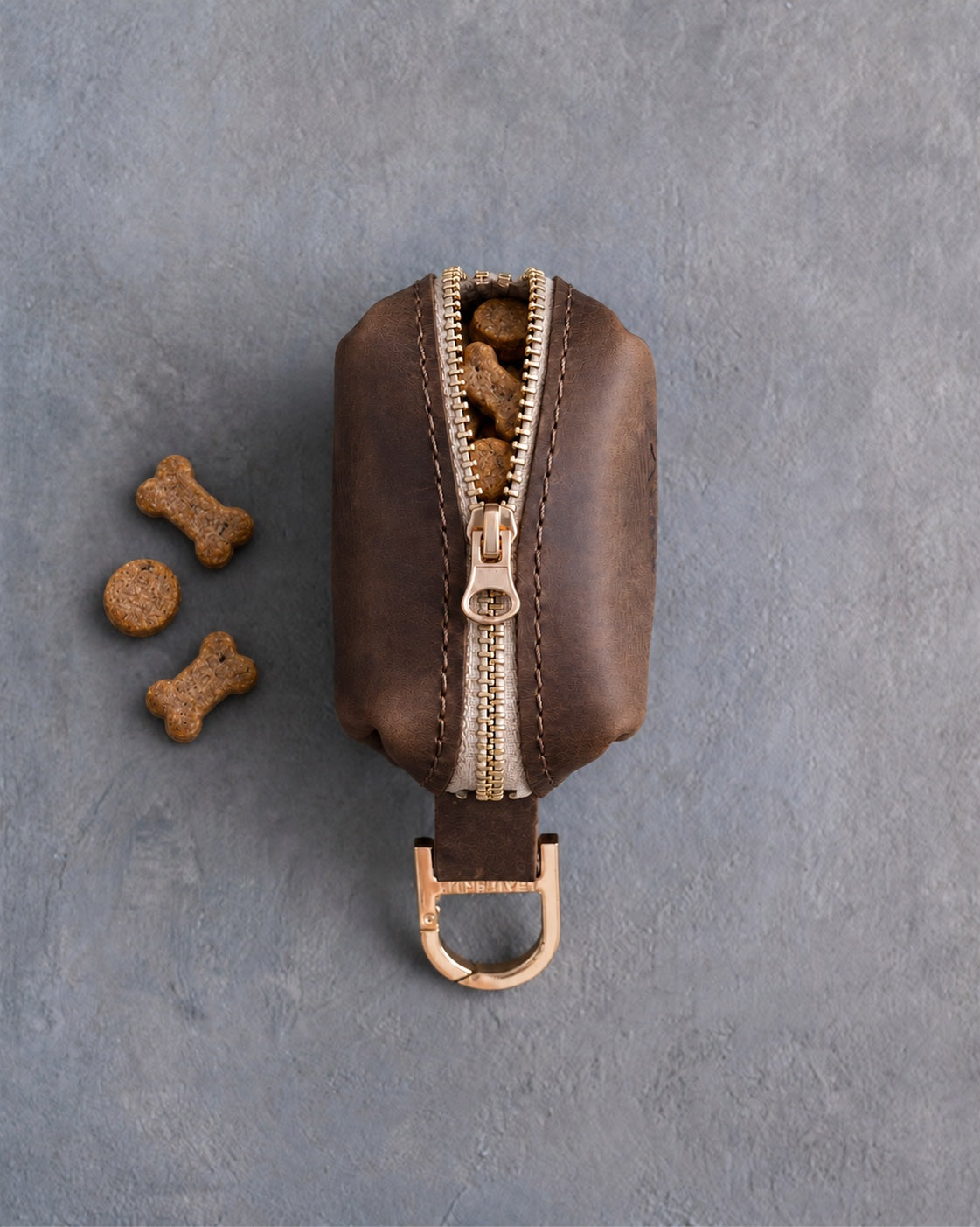 Brown leather zip treat pouch seen from the top, the zipper half open with small dog treats inside