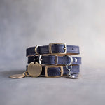 Blueberry navy leather dog collars stacked with pin buckles and a round engraved ID tag