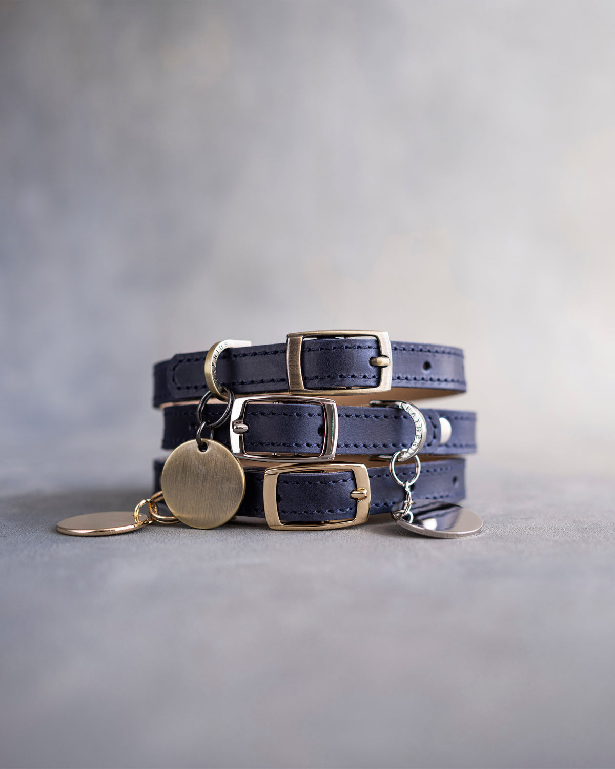 Blueberry navy leather dog collars stacked with pin buckles and a round engraved ID tag