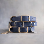 Blueberry navy leather dog collars stacked with pin buckles and gold hardware, ID tag attached