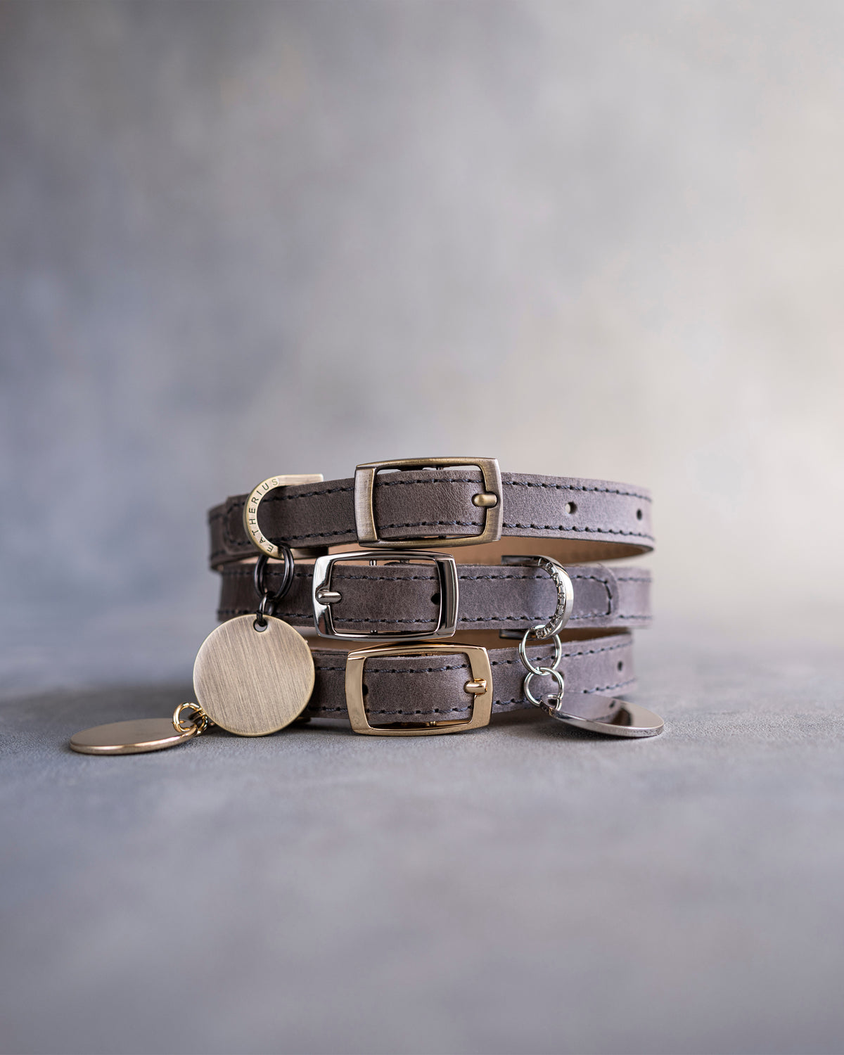 Country gray leather dog collars stacked with pin buckles and a round engraved ID tag