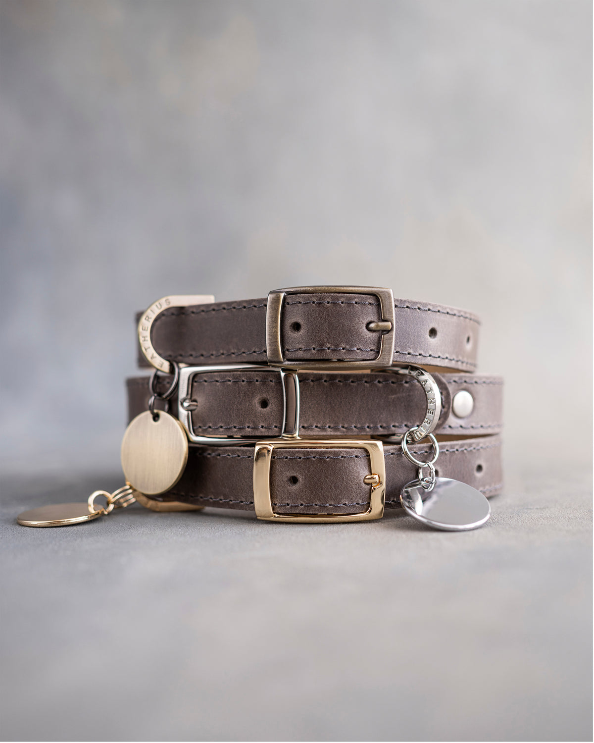 Country gray leather dog collars stacked with pin buckles and gold hardware, ID tag attached