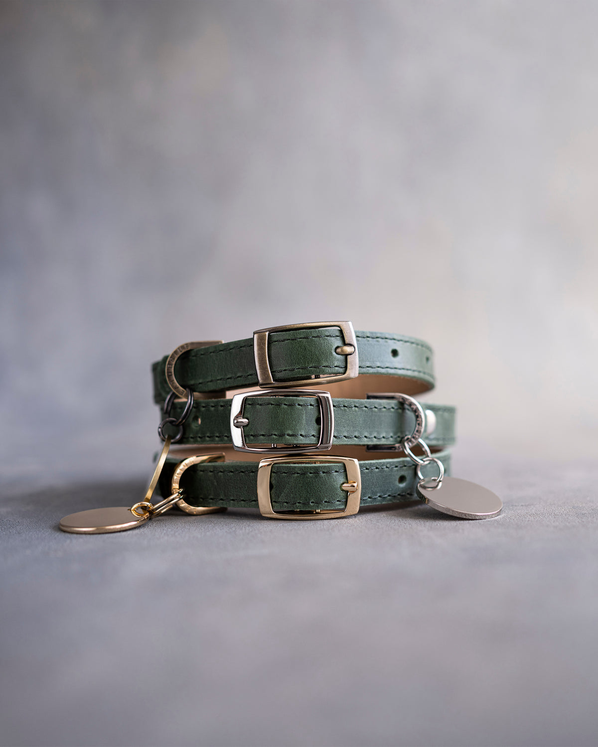 Forest green leather dog collars stacked with pin buckles and gold hardware, ID tag attached