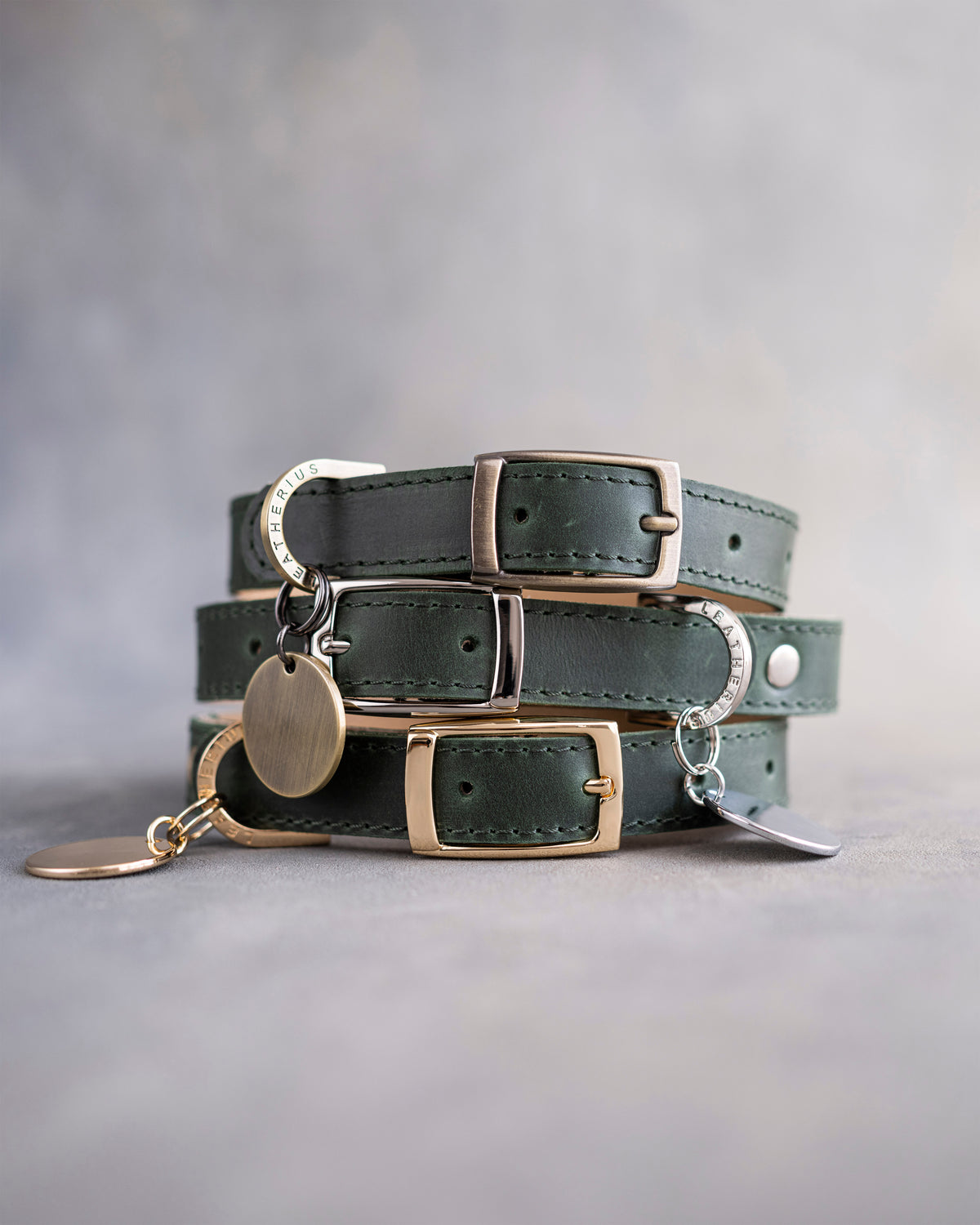 Forest green leather dog collars stacked with pin buckles and a round engraved ID tag