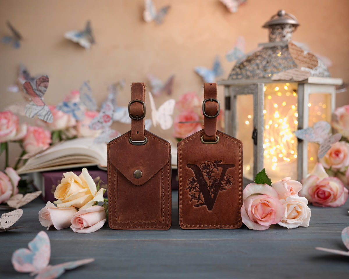 Arizona caramel leather luggage tag showing the floral initial front and address-card back, staged with roses